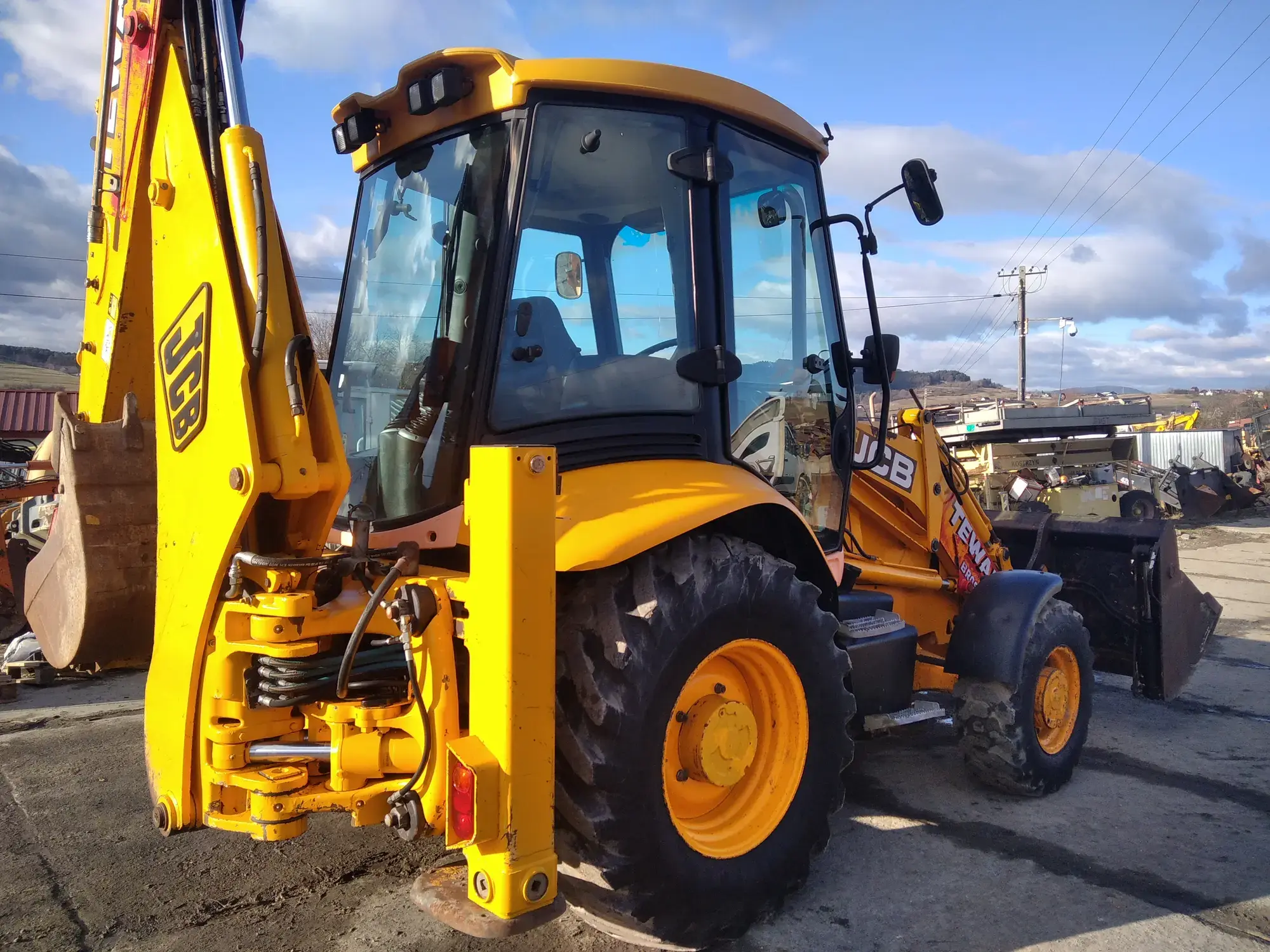 Koparko-ładowarka JCB 3CX od tyłu: ramię koparki z łyżką, kabina, a z przodu łyżka ładowarki
